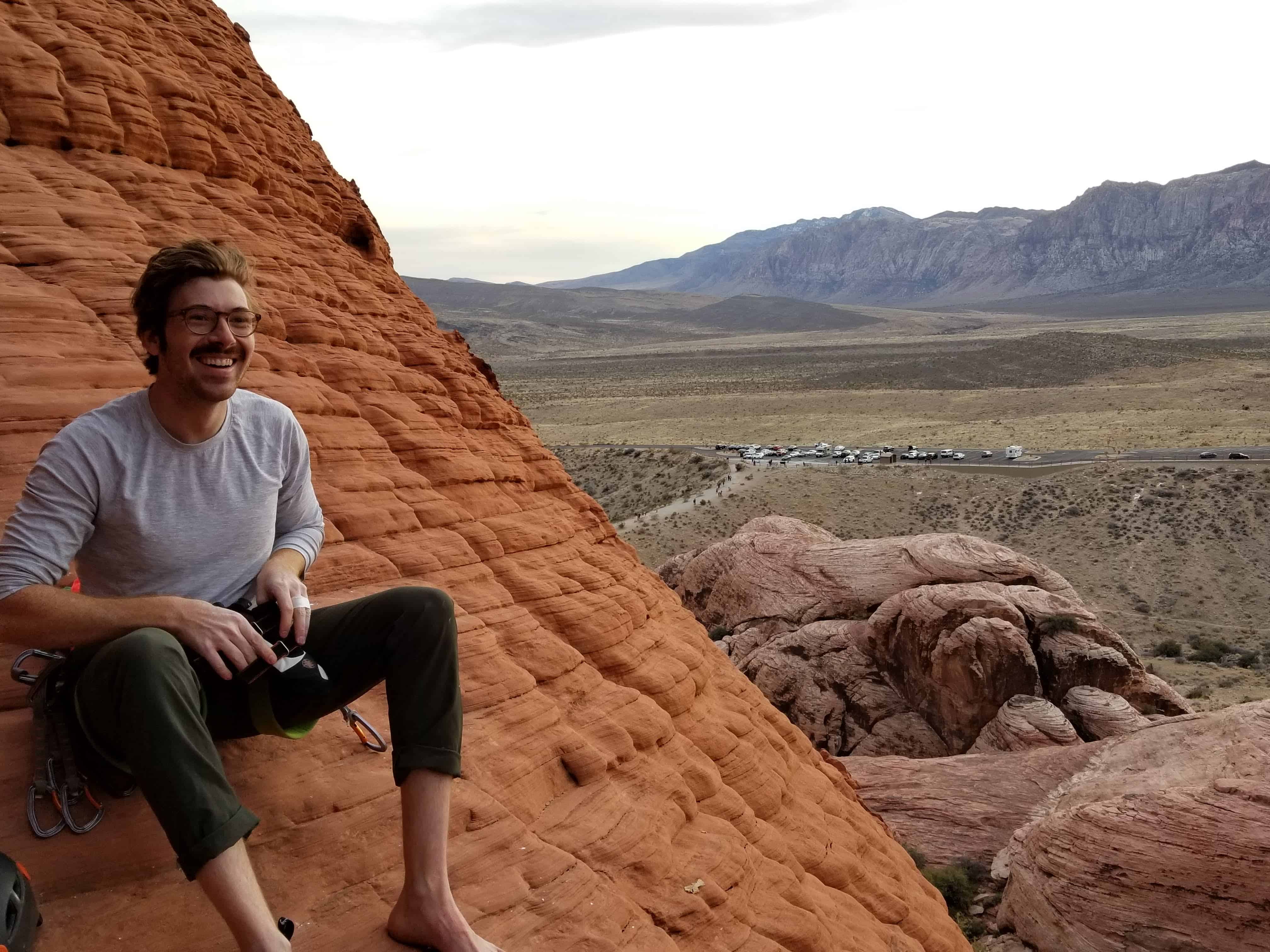 Sam sitting on a sandstone formation preparing for a sport climb.